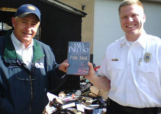 After a fire in the Durham County, NC Library shed, Supervisor Ronald Butler and Fire Marshall Michael Webb hold a rescued copy of Fire Sale. 